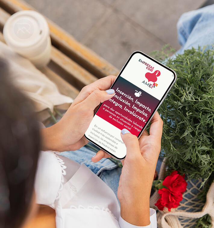 Madrileña con la compra de clavel rojo descansando en un banco mientras en primer plano vemos en su móvil la web de AMEI Somos empresas con i.